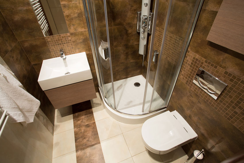 bagno moderno di piccole dimensioni con water, lavandino e box doccia, rivestimento con piastrelle marrone.